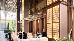 Un área de estar interior moderna con sofás y sillones, barandilla de madera y ventanas amplias con diseños geométricos.