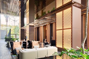 Un área de estar interior moderna con sofás y sillones, barandilla de madera y ventanas amplias con diseños geométricos.