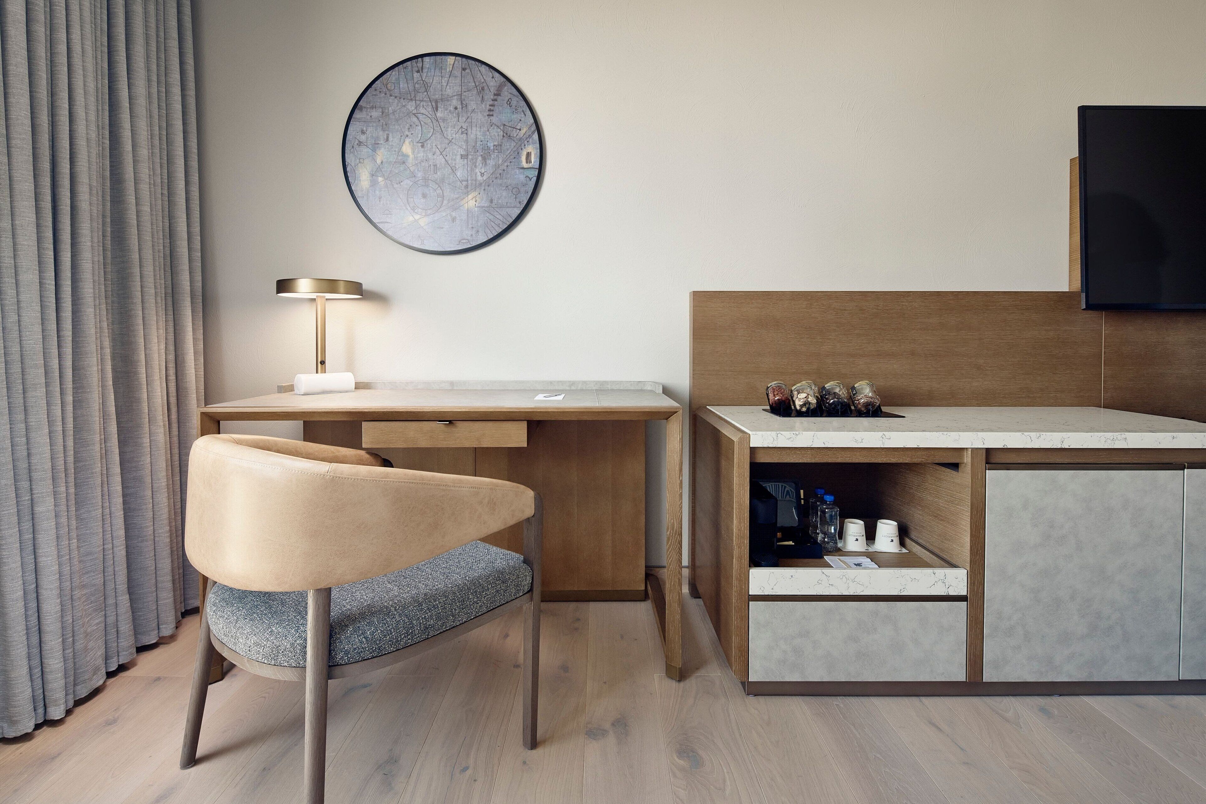 A modern hotel room with a wooden desk, a comfortable chair, a flat-screen TV, and a map artwork on the wall.
