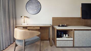 A modern hotel room with a wooden desk, a comfortable chair, a flat-screen TV, and a map artwork on the wall.