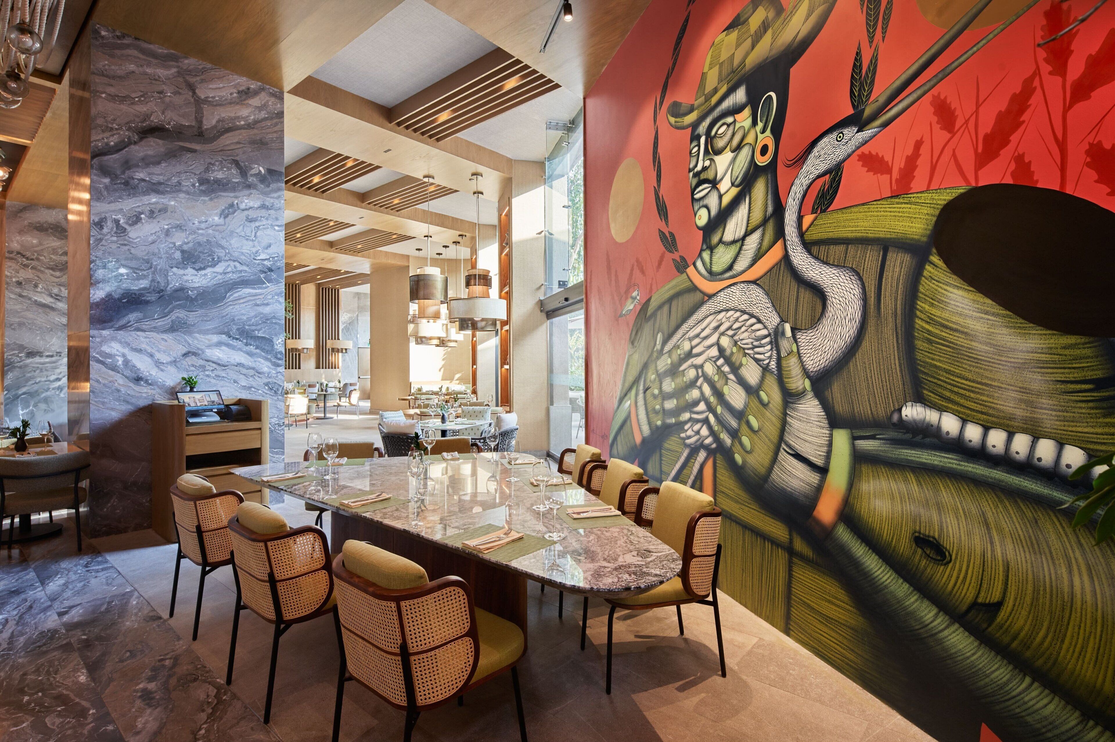 A modern dining area with a marble table, wicker chairs, and a large mural on the wall.
