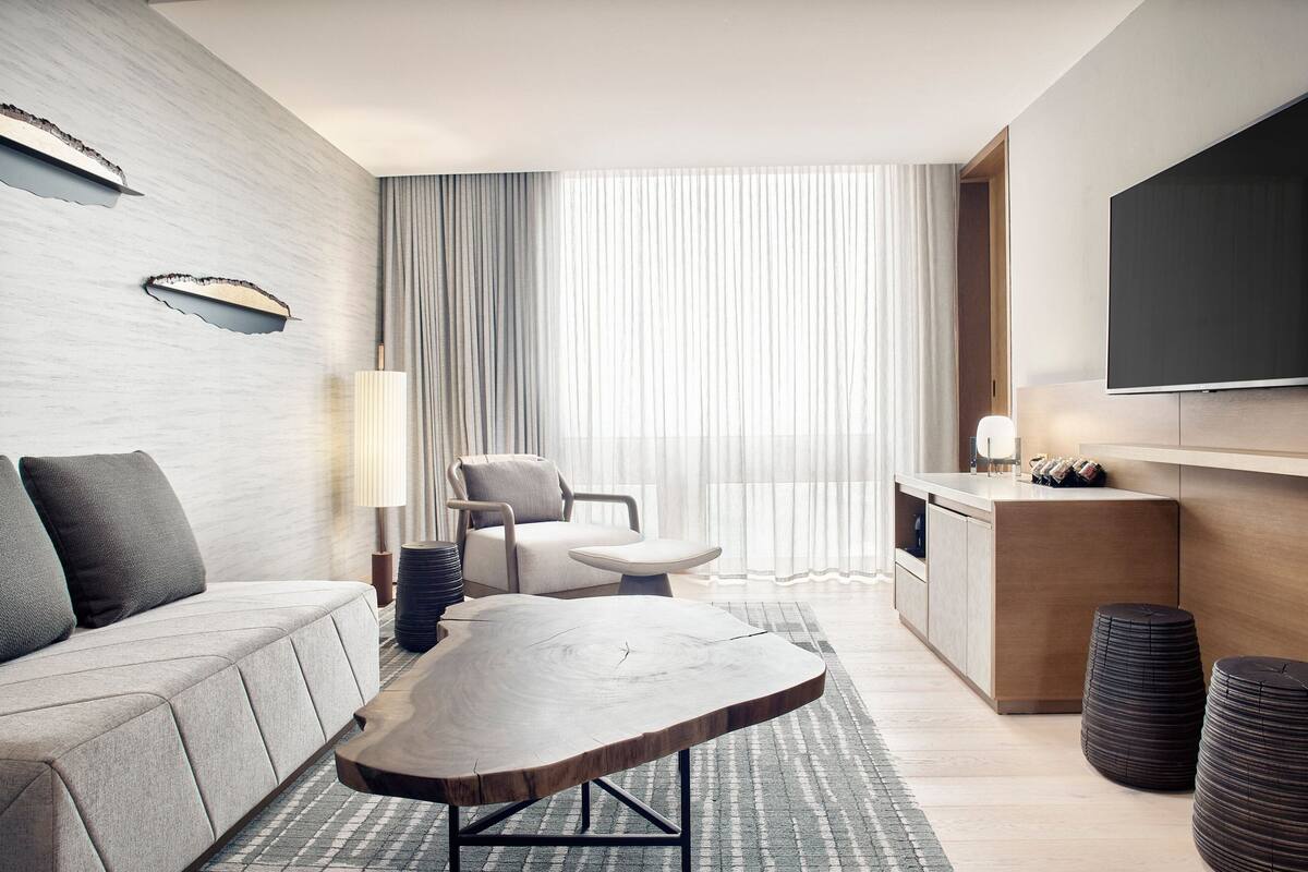 Een moderne hotelkamer met een bank, een houten bijzettafeltje, een stoel, een televisie en een kleine kitchenette.