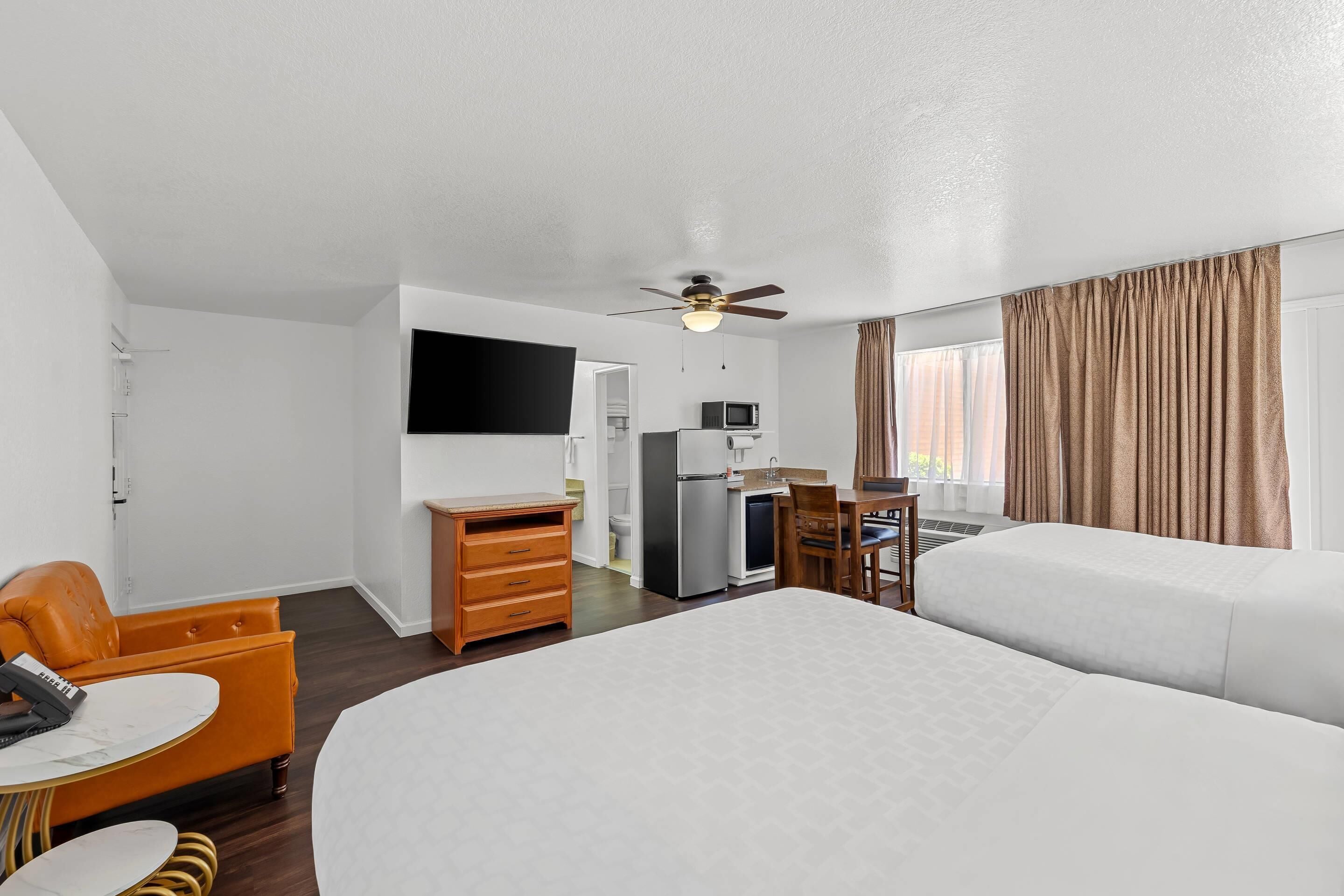 A hotel room with a bed, a desk, a chair, a television, a ceiling fan, and a window with curtains.