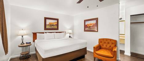 A hotel room with a bed, a chair, a ceiling fan, and two framed pictures on the wall.