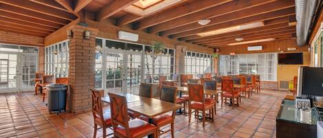 A spacious indoor dining area with wooden tables and chairs, a tiled floor, and a high ceiling with exposed beams.