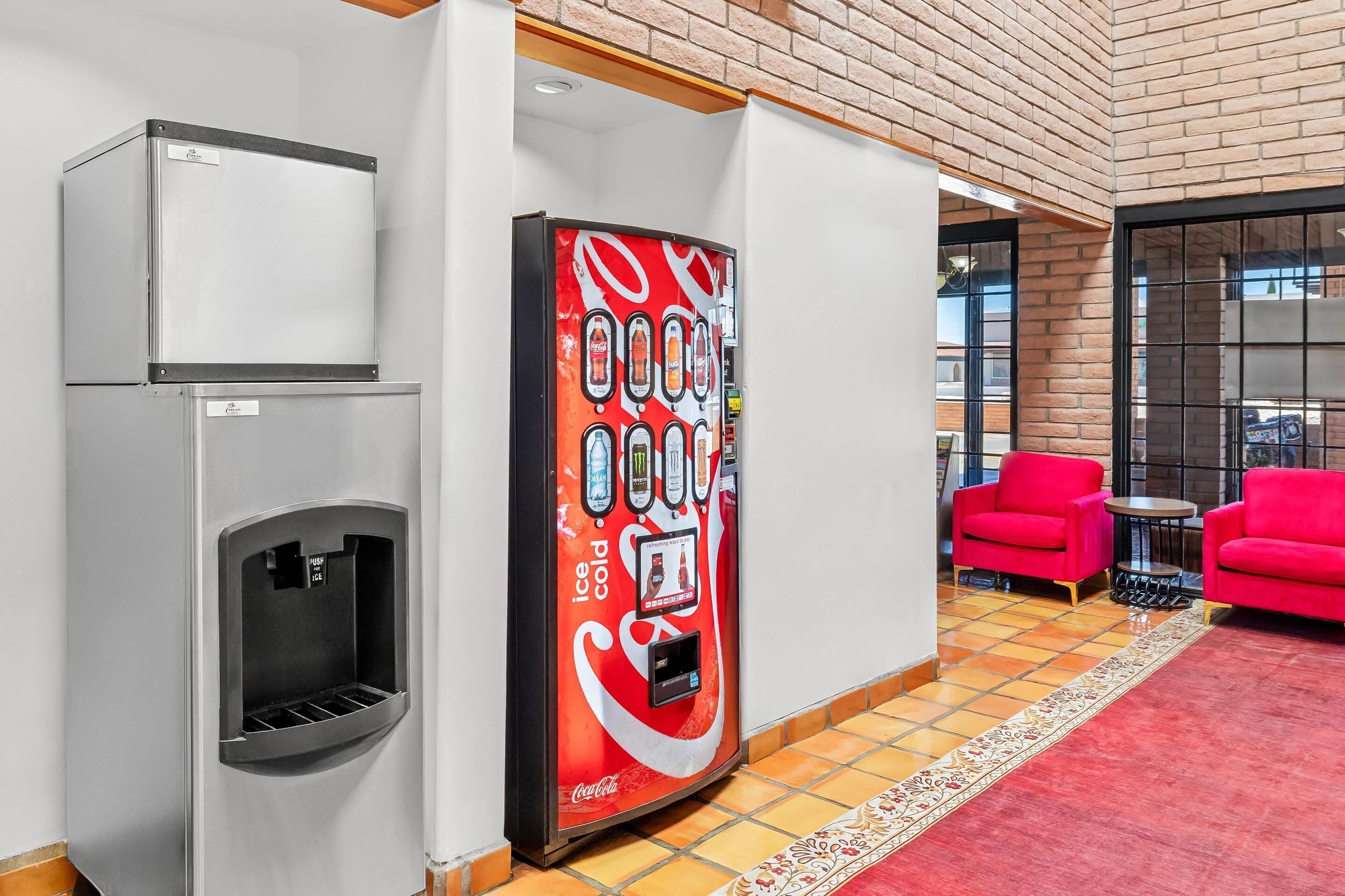 Máquina expendedora con logotipo de Coca-Cola, dispensador de agua y una zona de estar con sillas rojas y una pequeña mesa.