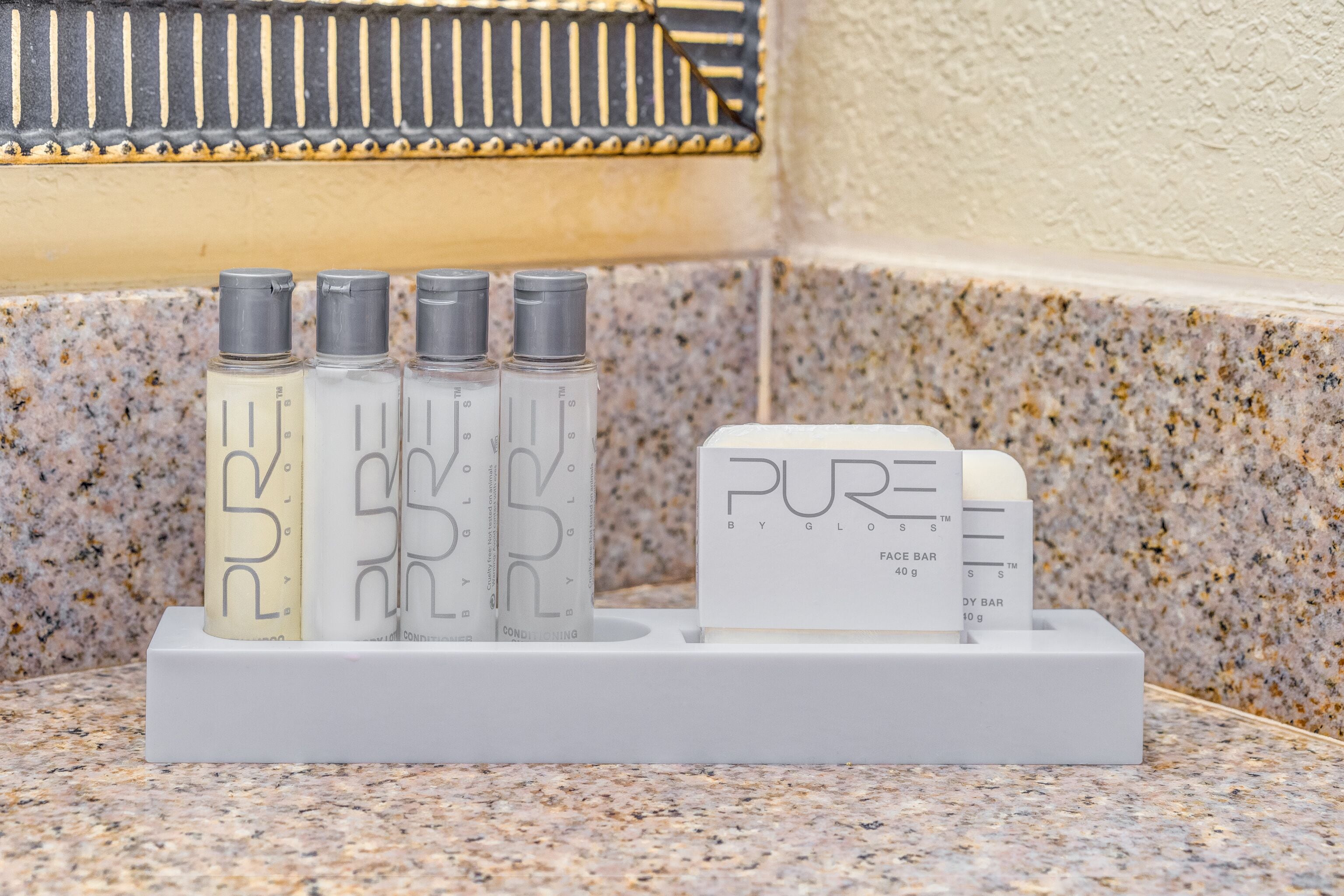 A set of four bottles and a bar of soap on a white stand against a speckled granite countertop.