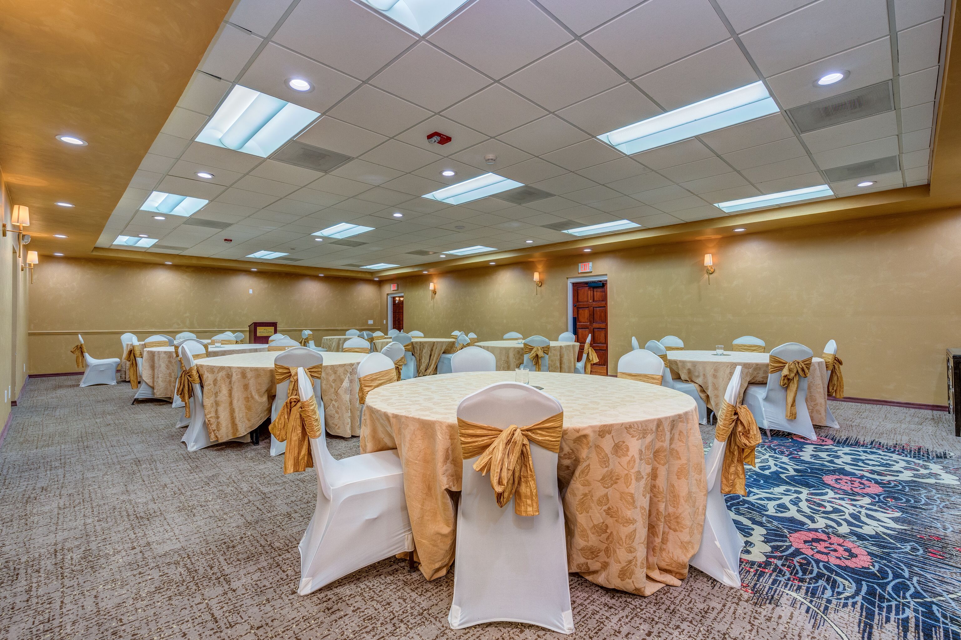 A conference room with round tables, white chairs, and gold sashes.