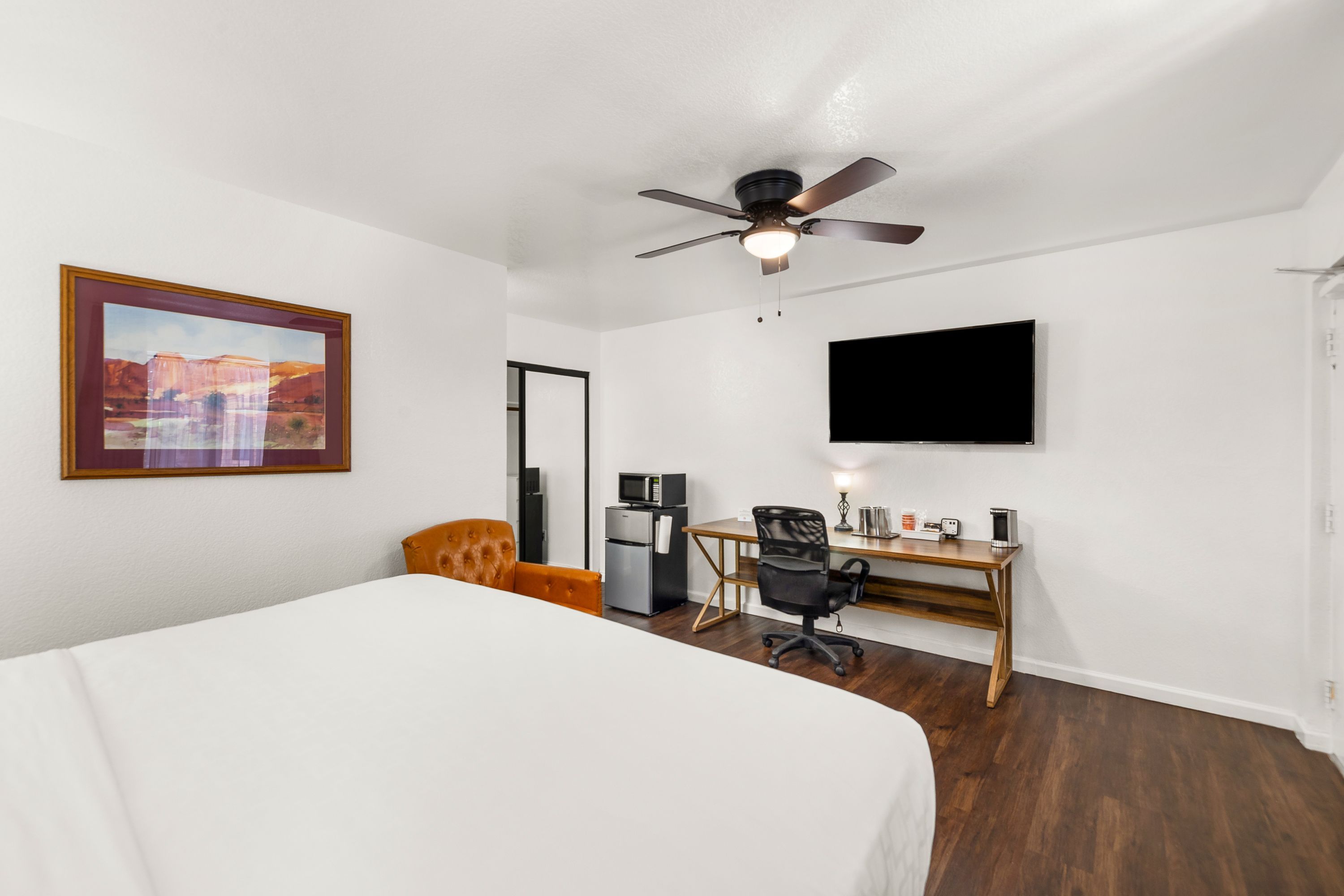Habitación de hotel con cama, escritorio con computadora, silla, televisor y ventilador de techo.