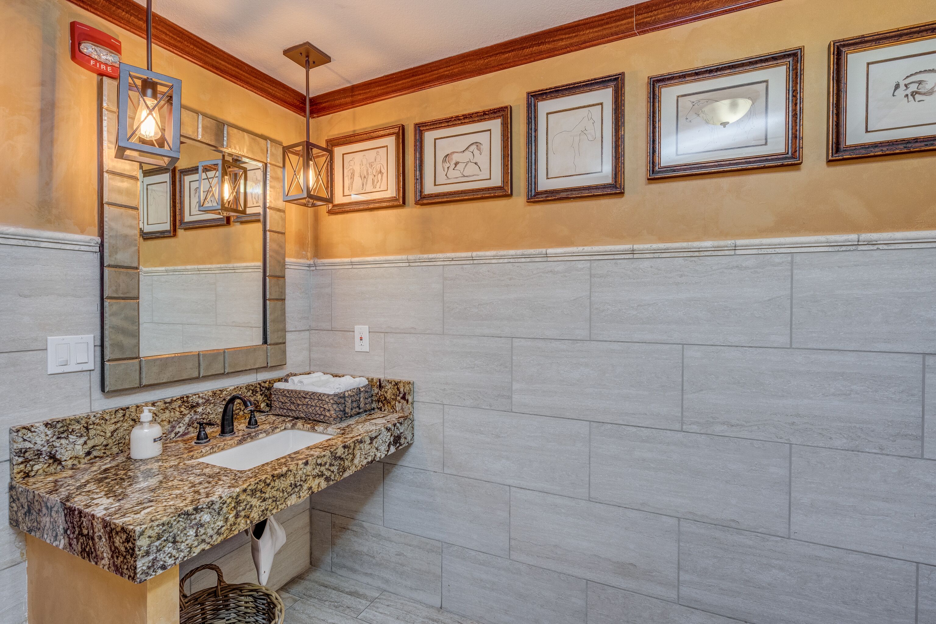 Une salle de bain avec un lavabo en granit, un grand miroir et des œuvres d’art encadrées accrochées au mur.