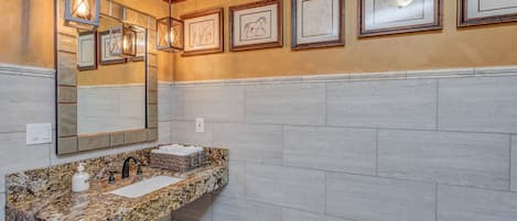 Une salle de bain avec un lavabo en granit, un grand miroir et des œuvres d’art encadrées accrochées au mur.