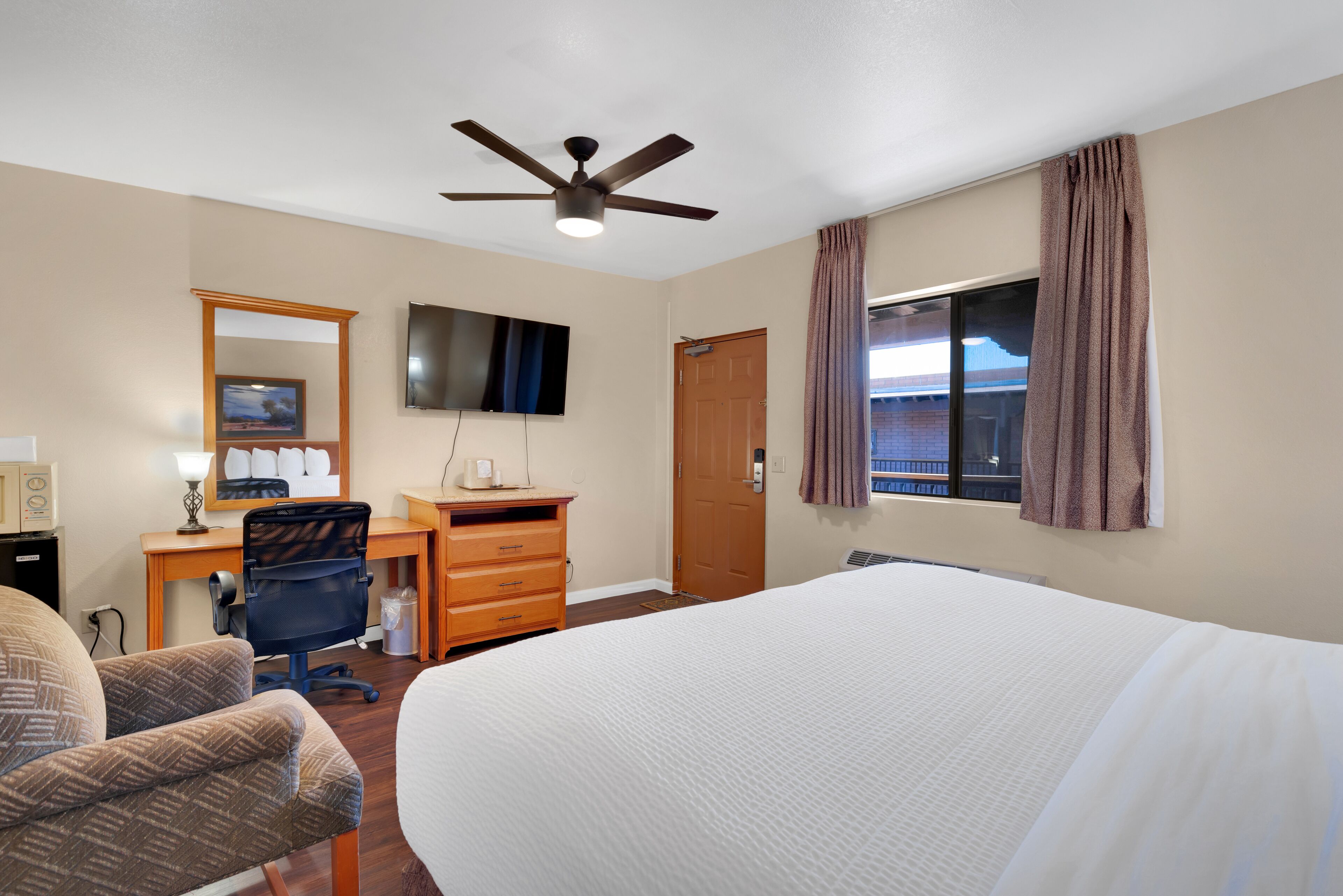 A hotel room with a bed, desk, chair, TV, and a ceiling fan.