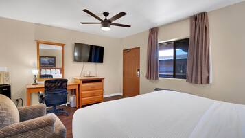 Una habitación de hotel con cama, escritorio, silla, televisión y ventilador de techo.