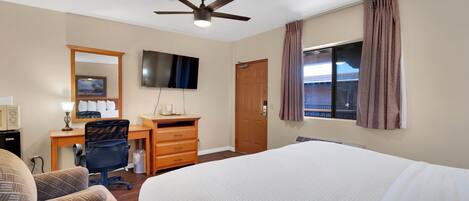 A hotel room with a bed, desk, chair, TV, and a ceiling fan.