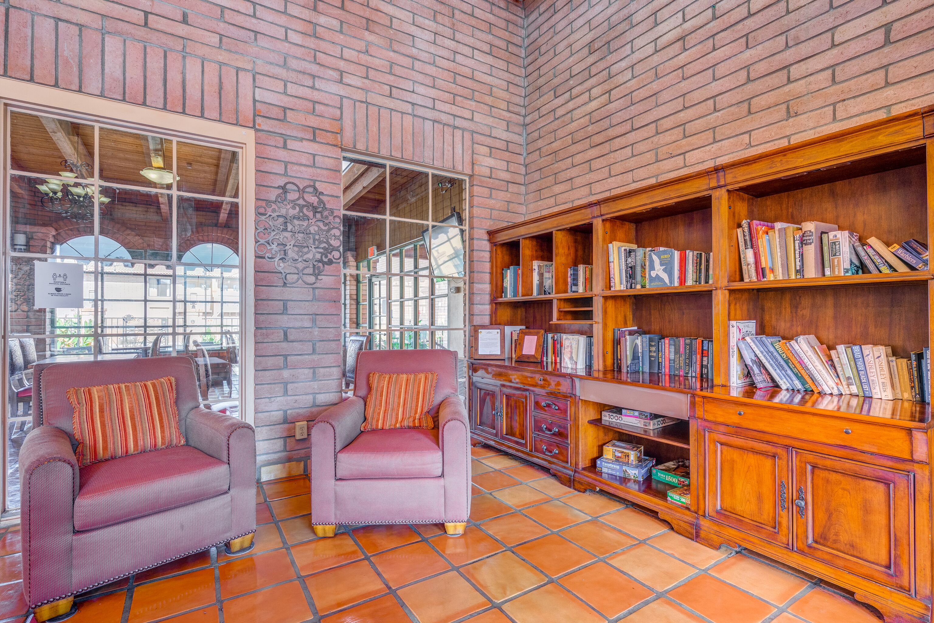 Un coin lecture confortable avec deux fauteuils, une bibliothèque en bois et un mur en briques.