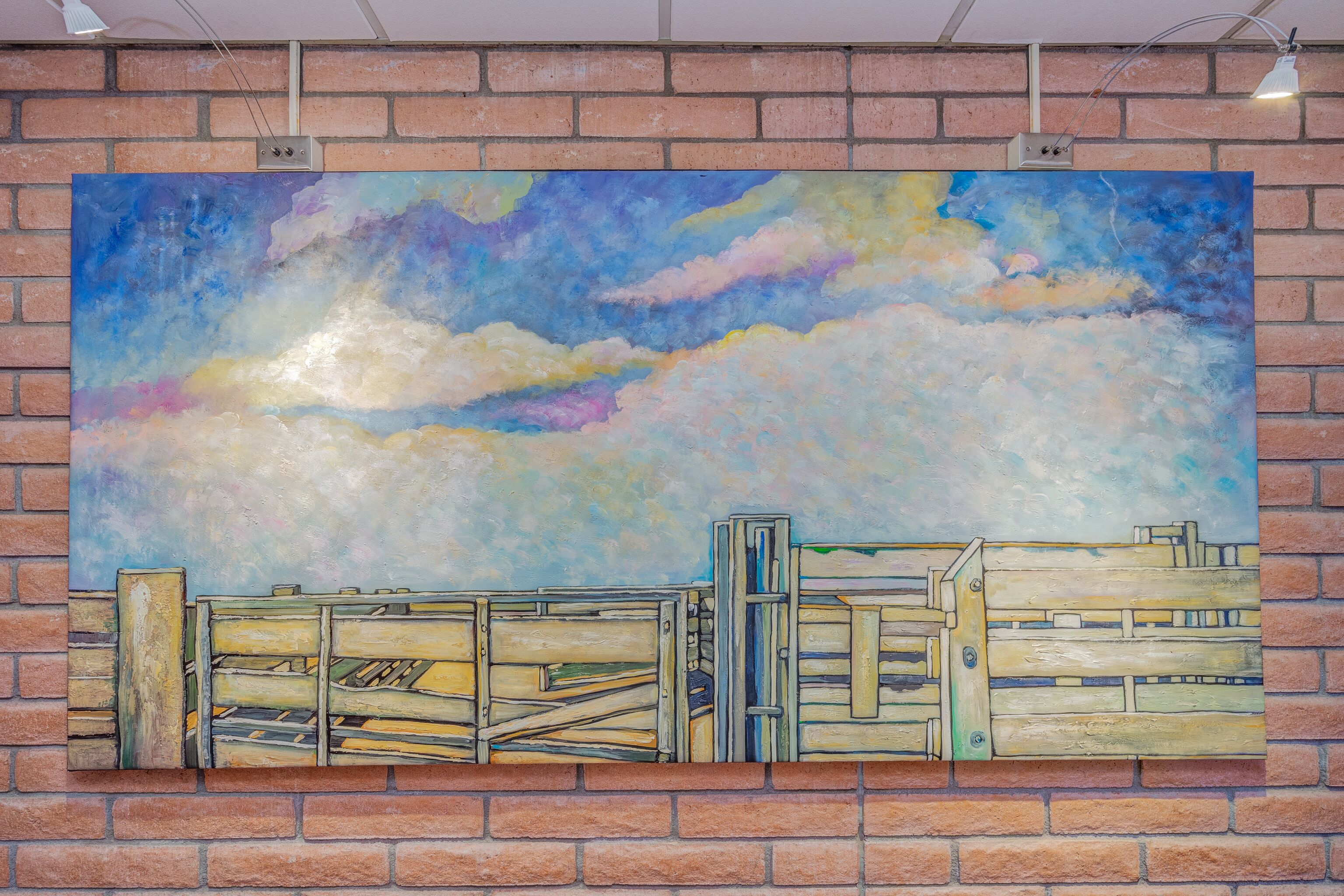 Una amplia pintura que muestra un cielo con nubes y una cerca de madera sobre un muro de ladrillo.