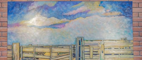 Una amplia pintura que muestra un cielo con nubes y una cerca de madera sobre un muro de ladrillo.