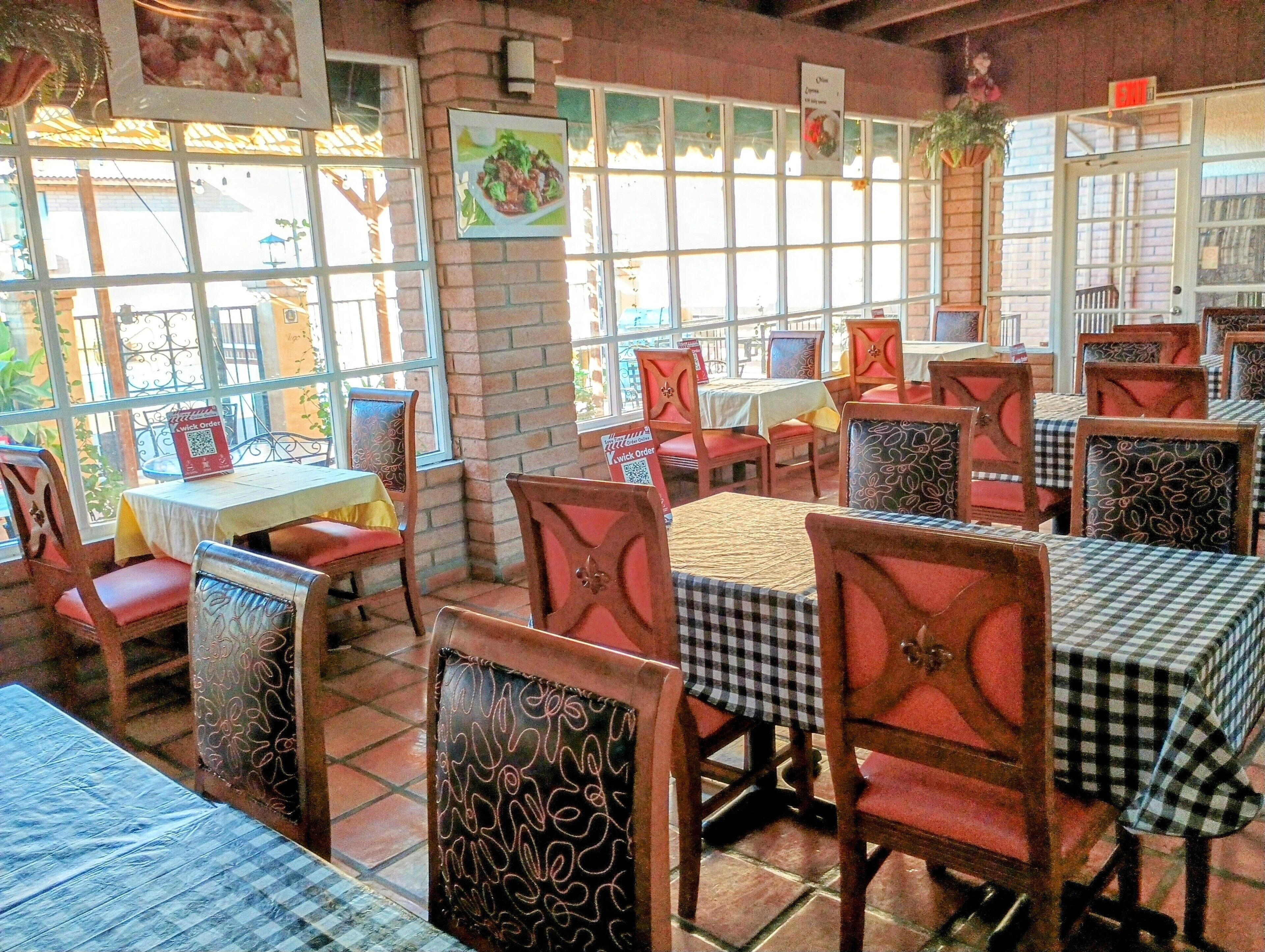 Un interior de restaurante con paredes de ladrillo, ventanas amplias y manteles a cuadros.