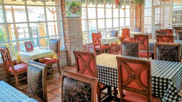 Un interior de restaurante con paredes de ladrillo, ventanas amplias y manteles a cuadros.