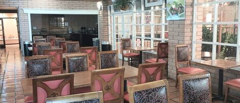 Een restaurant met bakstenen muren, houten tafels en stoelen, en grote ramen.