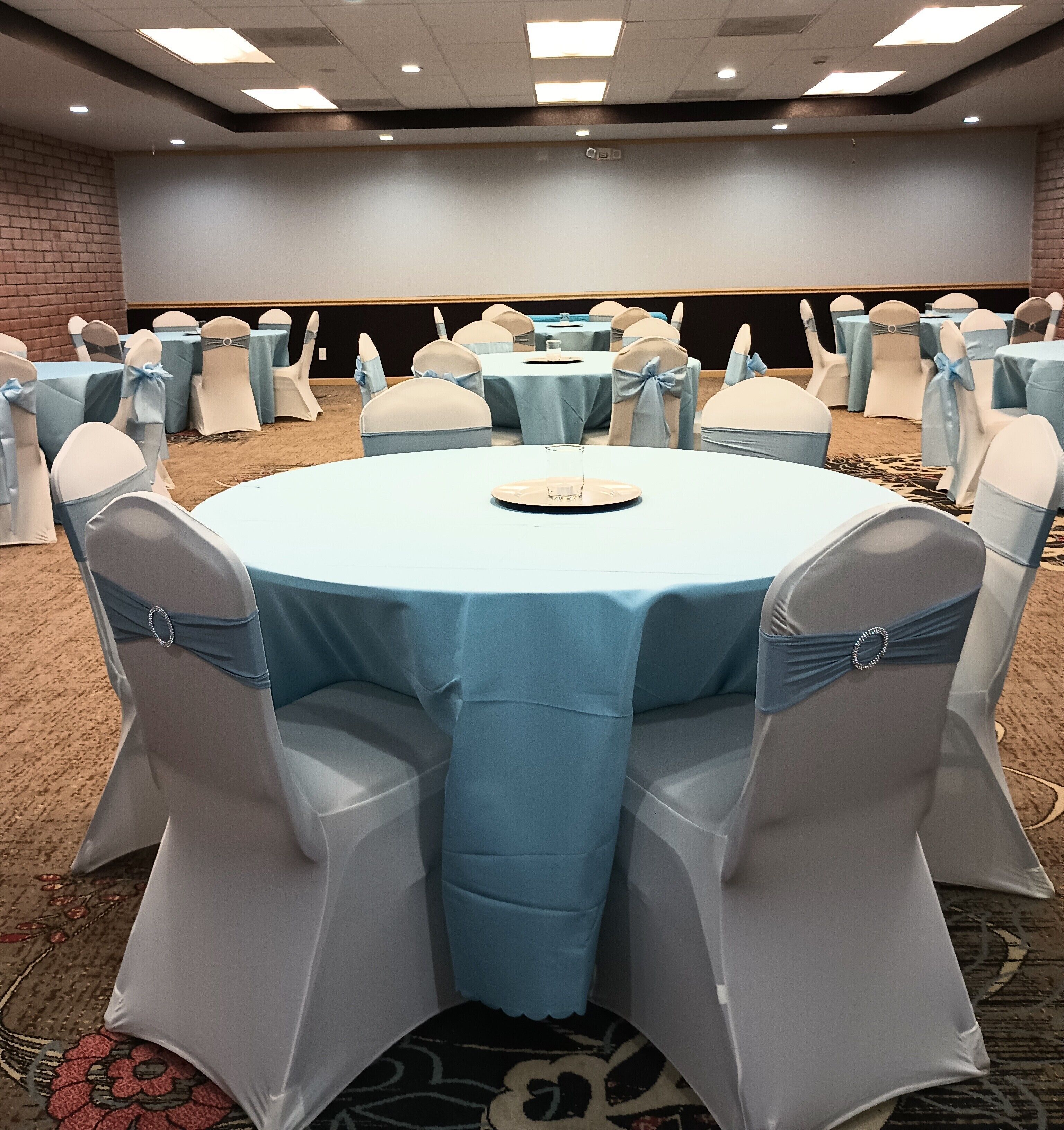 Une salle de conférence avec des tables rondes, des chaises ornées de rubans bleus et une scène en arrière-plan.