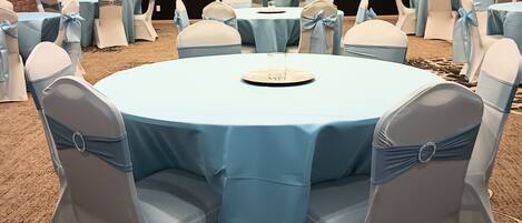 A conference room with round tables, chairs with blue sashes, and a stage in the background.