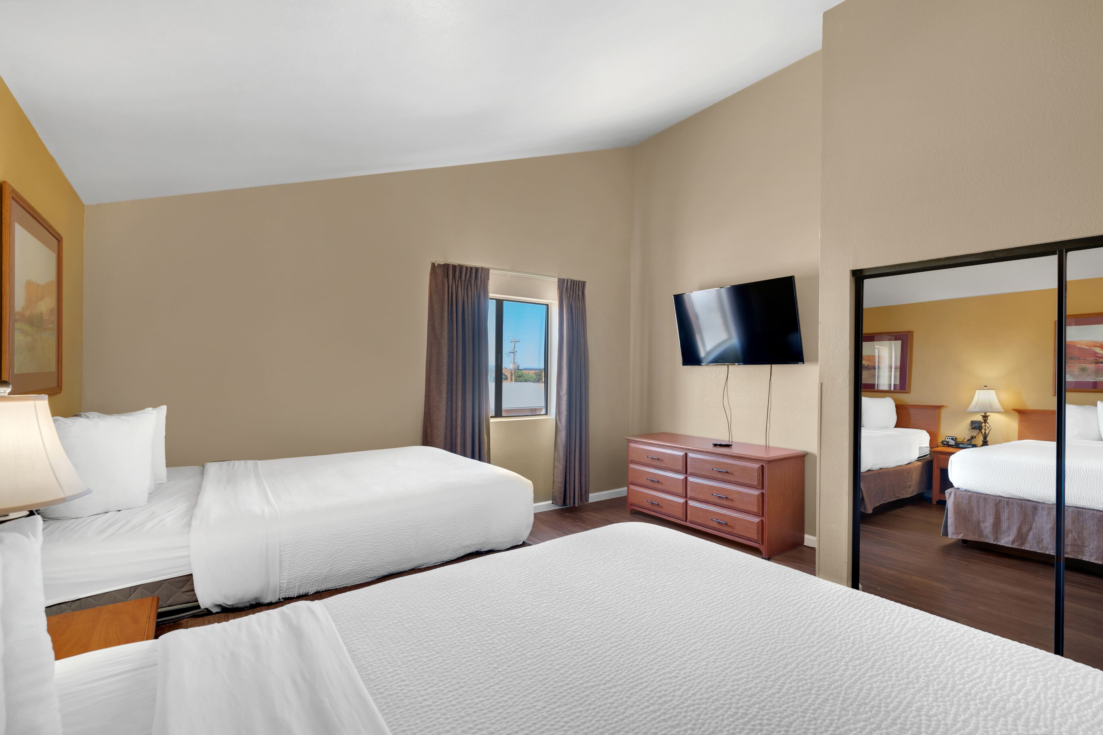 Quarto de hotel com duas camas, televisão, cômoda e janela com cortinas.