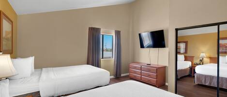 Quarto de hotel com duas camas, televisão, cômoda e janela com cortinas.