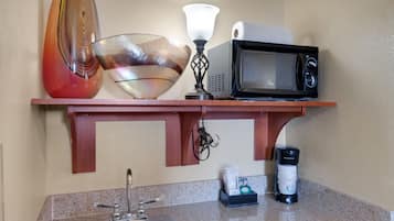 A kitchen with a sink, a microwave, a coffee maker, and decorative items on a shelf.
