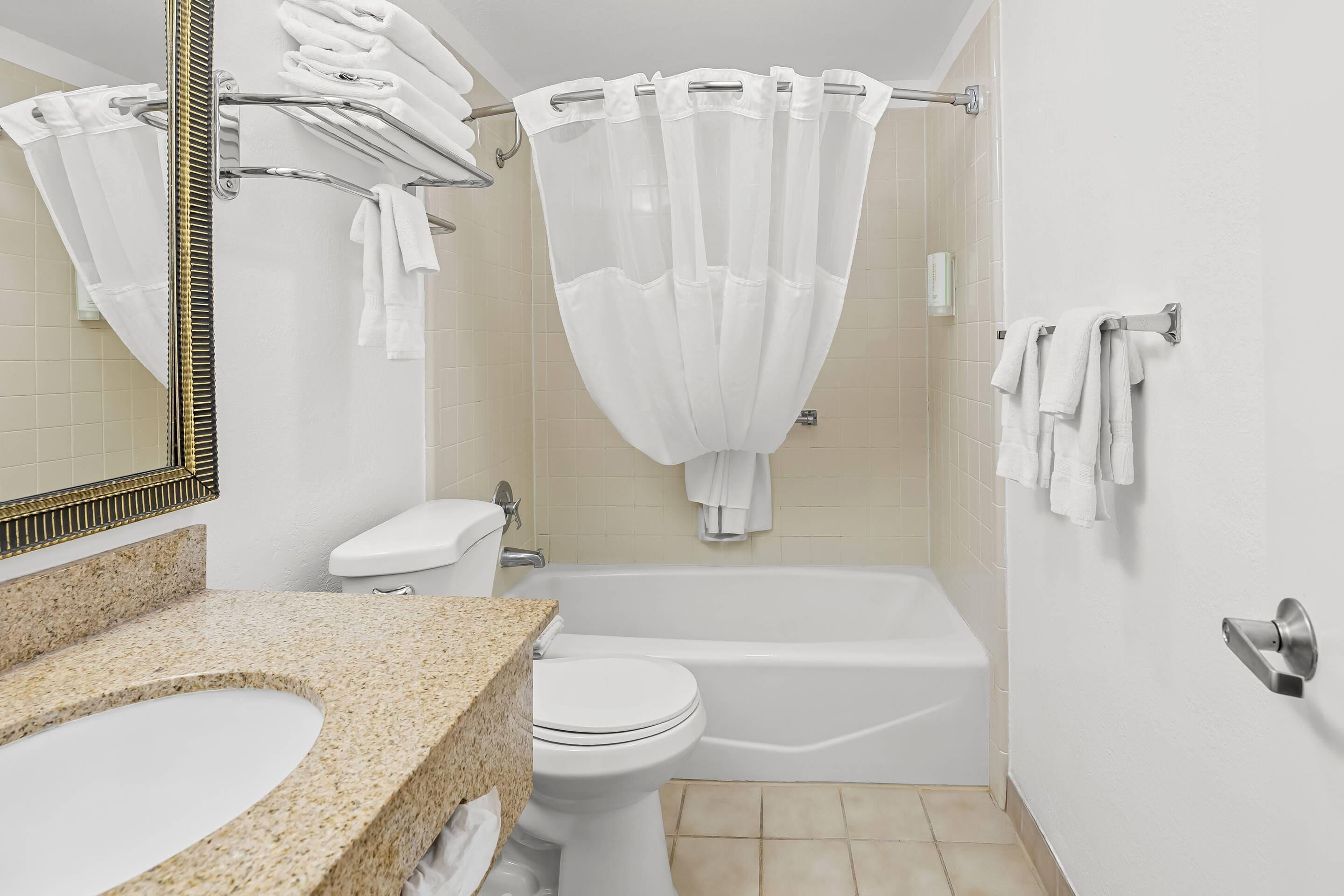 Un baño con encimera de granito, accesorios blancos, bañera y cortina de ducha.