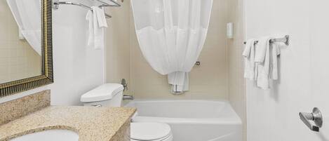 Un baño con encimera de granito, accesorios blancos, bañera y cortina de ducha.