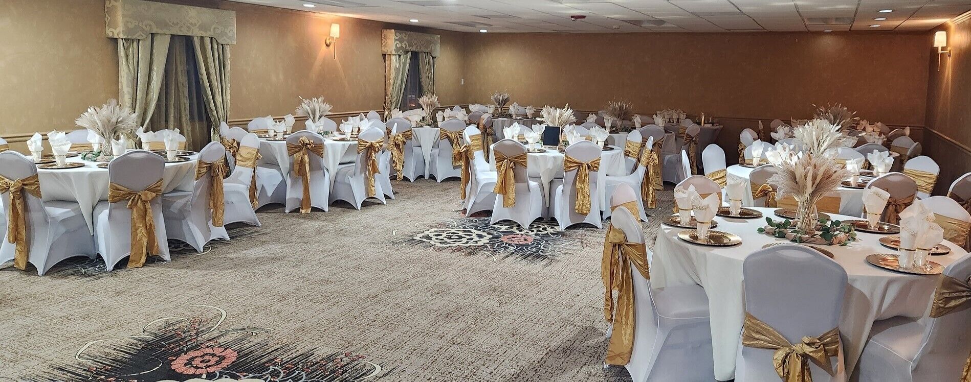 A banquet hall with round tables and chairs, each adorned with white tablecloths and gold sashes.