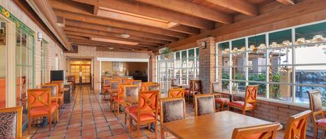 A restaurant with wooden tables and chairs, a tiled floor, and large windows.
