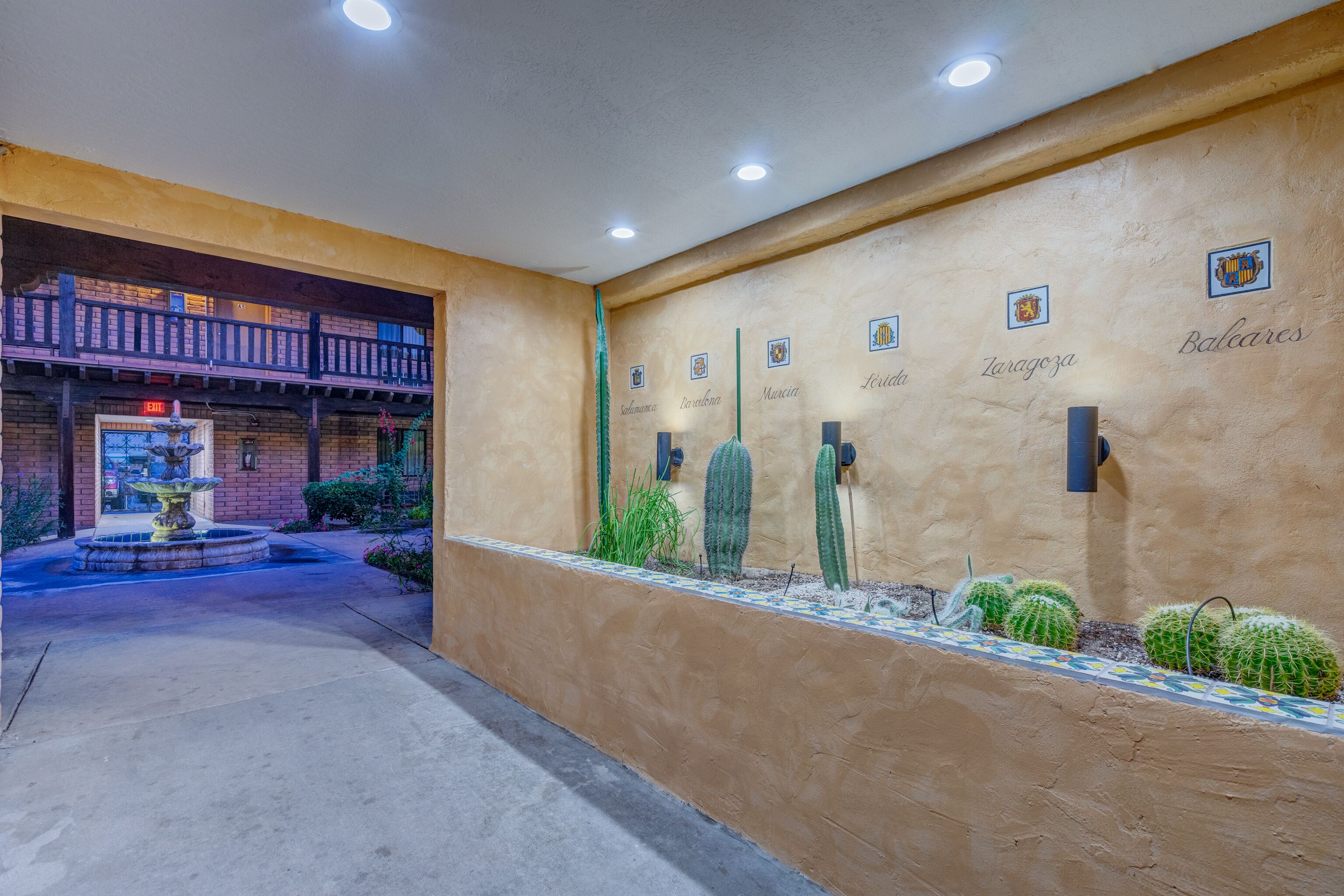 A courtyard with a fountain, cacti, and a wall with names of cities.