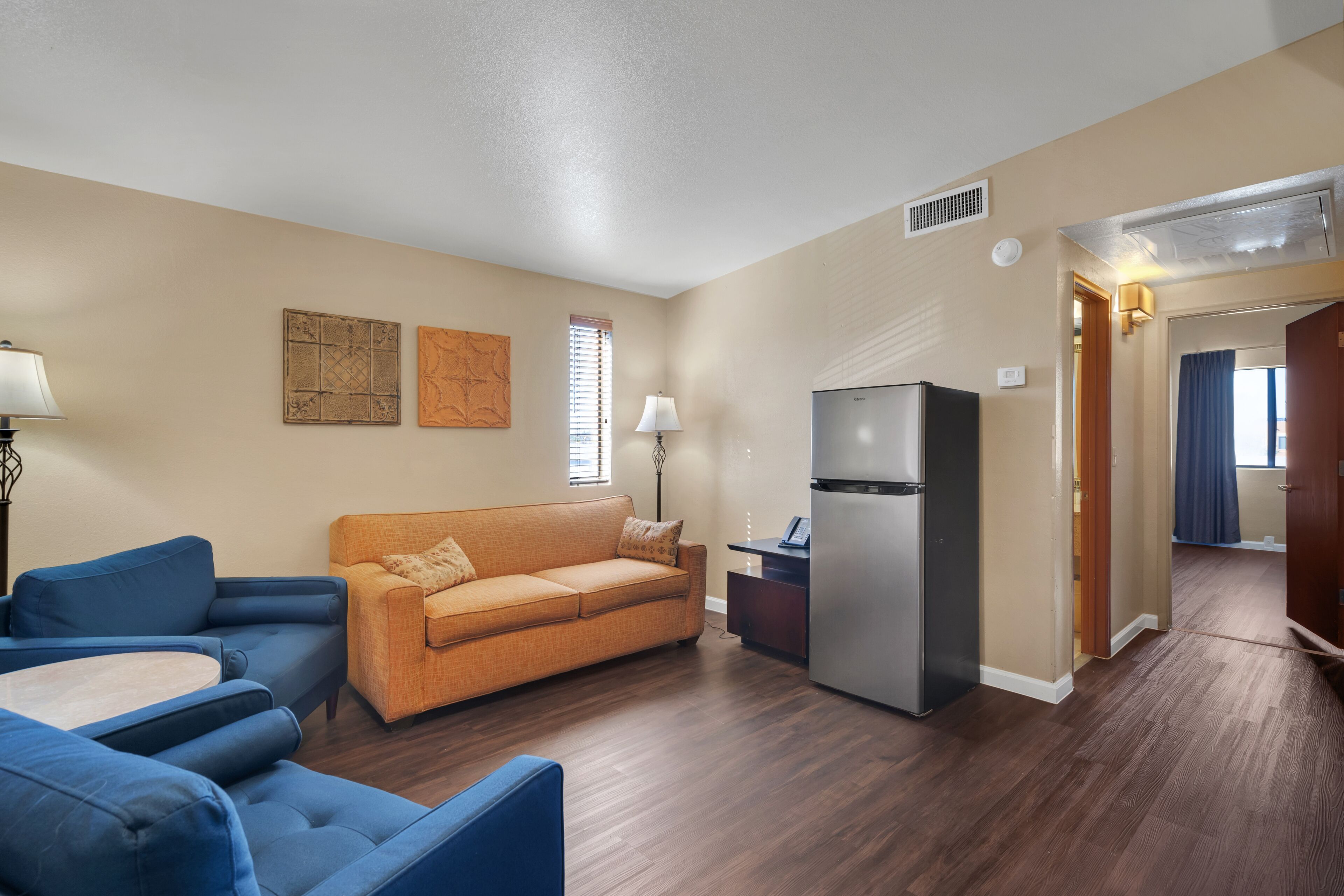 A compact living space with a sofa, a dining table, a refrigerator, and a lamp.