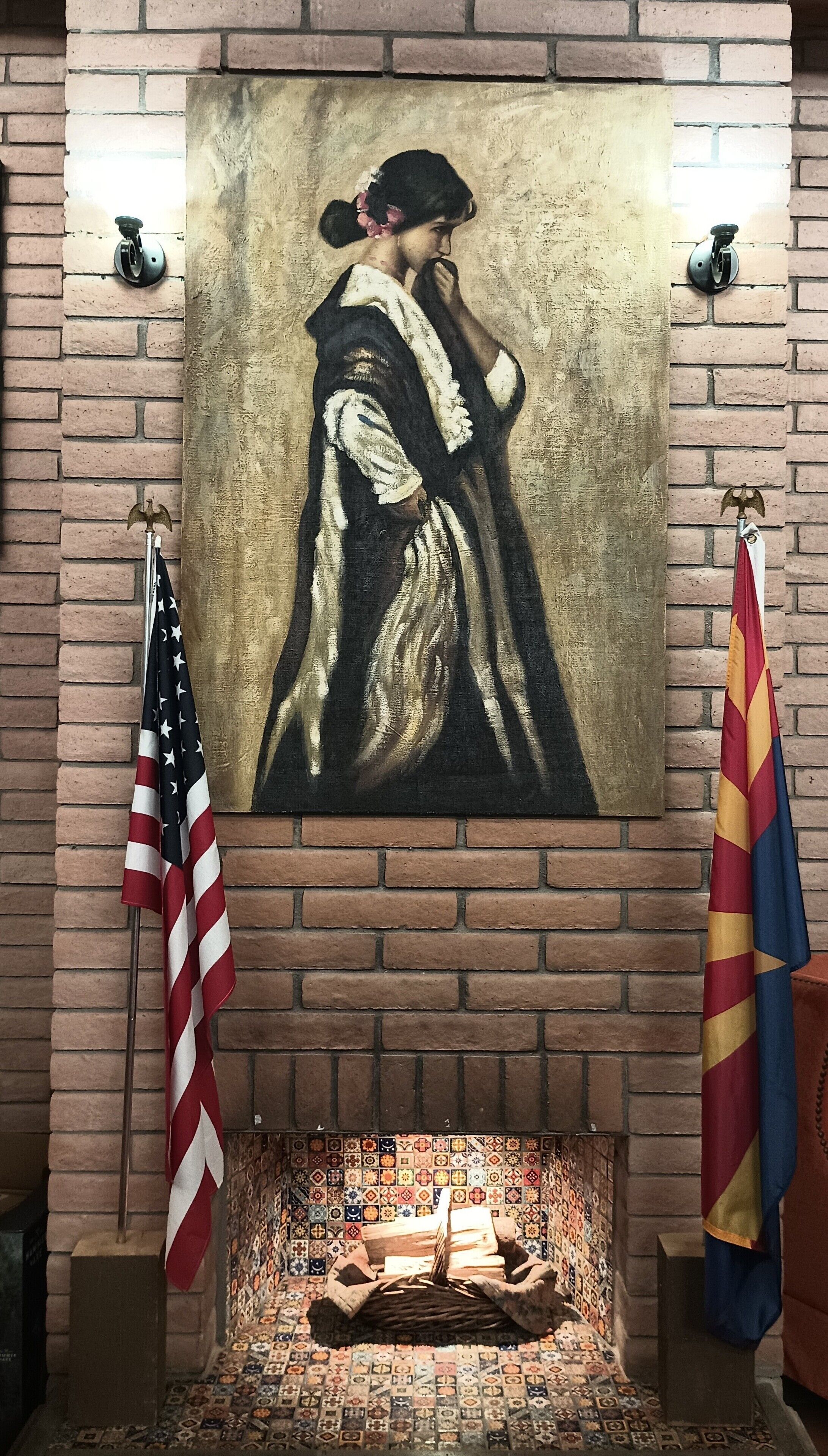 A fireplace with a tiled mosaic floor, a painting above it, and two flags on either side.