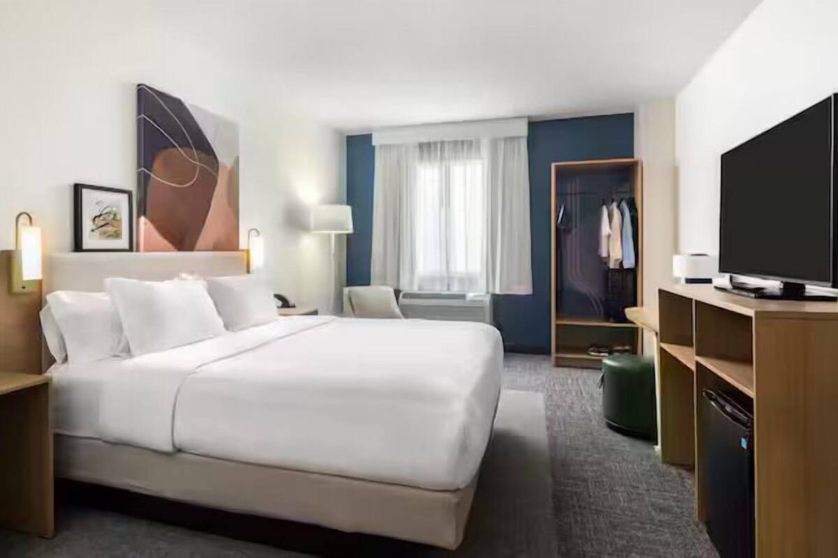 Habitación de hotel con una cama grande, mesitas de noche, televisión, armario y ventana con cortinas.