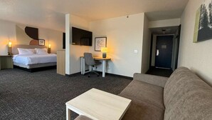 A hotel room with a bed, a desk, a chair, a sofa, and a small table.