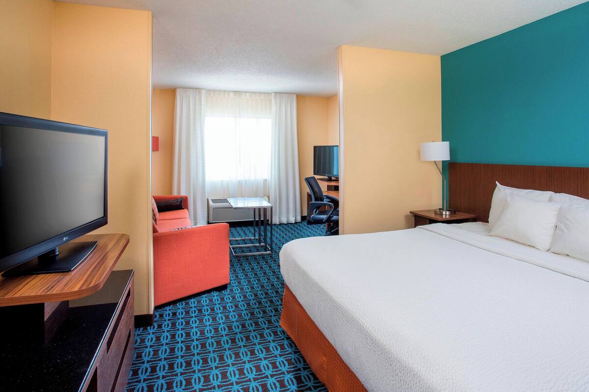 A hotel room with a large bed, a television on a wooden stand, a desk with a chair, and a small table.