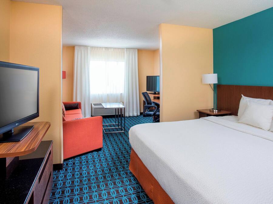 A hotel room with a large bed, a television on a wooden stand, a desk with a chair, and a small table.