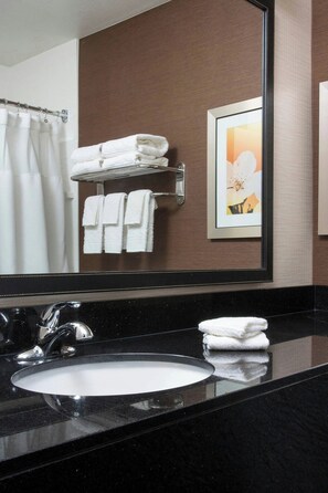 A bathroom with a black countertop, a white sink, a mirror, and a towel rack with folded towels.