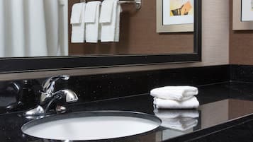 Un baño con encimera negra, un lavabo y un espejo que refleja un perchero con toallas.
