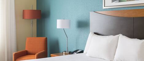 A hotel room with a bed, a chair, a nightstand with a lamp, and a framed picture on the wall.