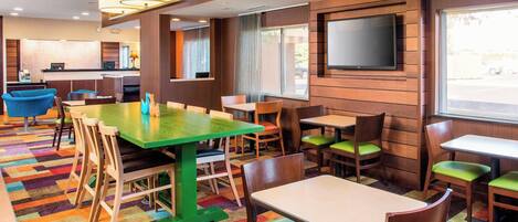 A restaurant with a colorful carpet, wooden walls, and a flat-screen TV mounted on the wall.