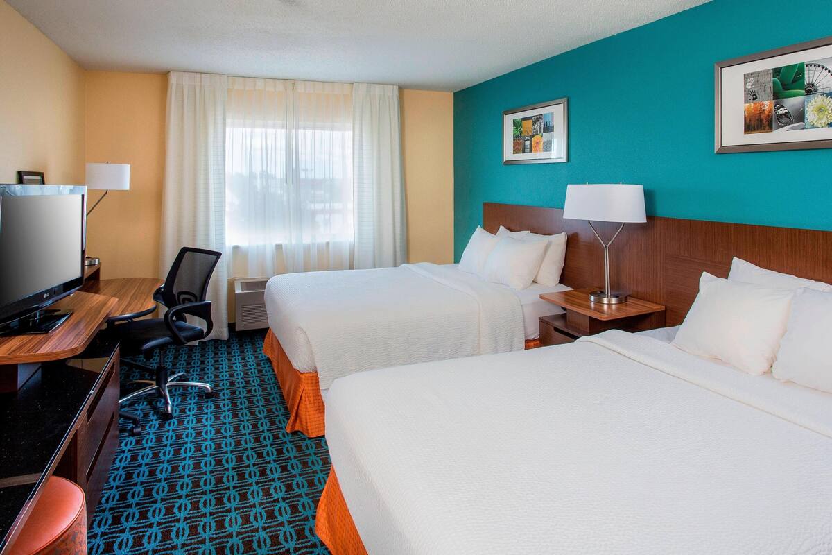 A hotel room with two beds, a desk with a computer, a chair, and a TV.