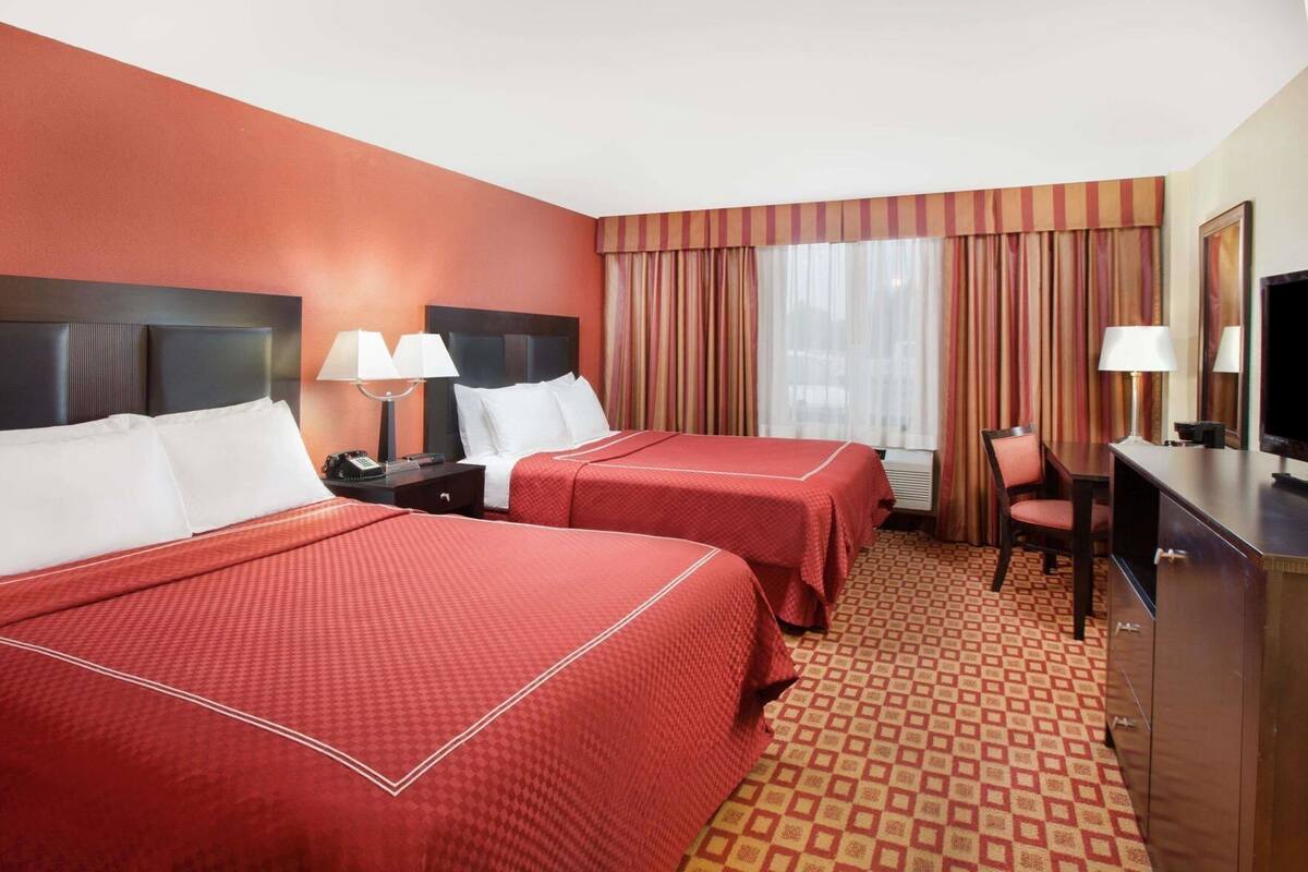 A hotel room with two beds, a desk, a chair, a TV, and a window with curtains.