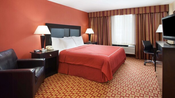 A hotel room with a large bed, two bedside tables with lamps, a desk with a chair, and a television. - Super 8 by Wyndham Chicago Northlake O'Hare South (Northlake)