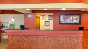 A reception desk with a wooden finish, framed artwork on the wall, and a clock. - Super 8 by Wyndham Chicago Northlake O'Hare South (Northlake)