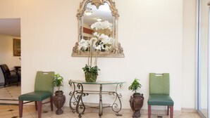 A reception area with a glass-top table, two green upholstered chairs, a decorative mirror, and potted plants. - Super 8 by Wyndham Chicago Northlake O'Hare South (Northlake)