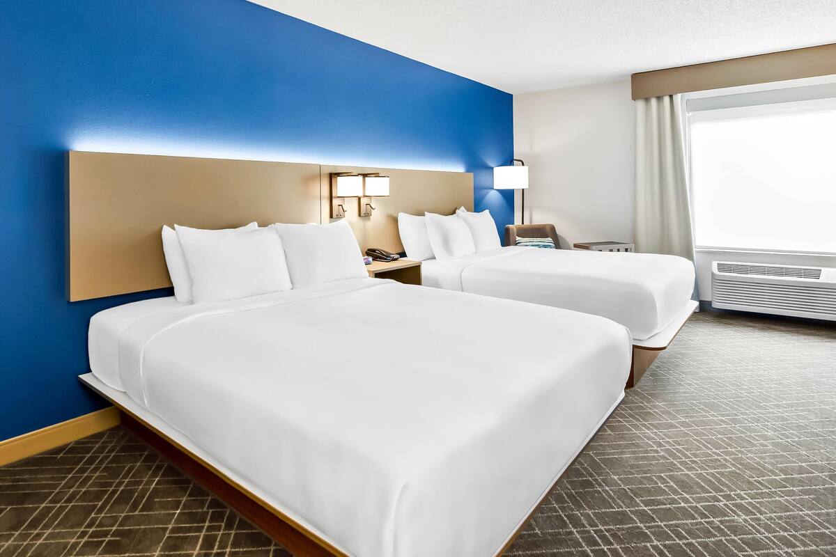 A hotel room with two beds, a nightstand, a lamp, and a window with curtains.